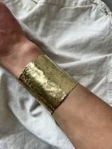 Brazalete ancho de metal plateado con textura martillada.