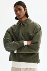 Campera de algodón en color verde militar, con cuello camisero, cierre frontal, un bolsillo superior con cierre y dos bolsillos laterales ribeteados.