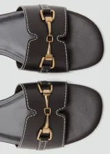 Sandalias planas de color negro con puntera redondeada, tira ancha con costuras blancas a contratono y detalle metálico dorado en el empeine.