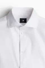 Camisa de algodón blanca con cuello italiano, cierre frontal de botones y mangas largas con puños ajustables. Corte entallado Slim Fit.