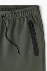 Pantalón de jogging deportivo color verde oscuro, de corte ajustado (slim fit), confeccionado en tejido funcional DryMove™ que absorbe el sudor. Presenta cintura elástica con cordón de ajuste y bolsillos laterales con cierre sellado.