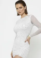 Vestido corto de manga larga, color blanco con estampado de puntos brillantes plateados. Presenta un diseño ajustado al cuerpo con cuello redondo.