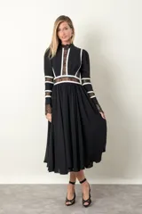 Vestido midi negro con cuello mao, mangas largas con puños de encaje y falda amplia con tul. Presenta encaje con transparencia en el pecho y vivos blancos en cuello, mangas y cintura.