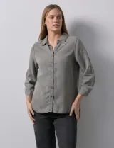 Camisa gris de tencel con cuello con solapa, escote en V y abertura central con botones. Largo de manga regulable con presilla y botón. Ruedo en espalda con tajo.