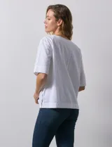 Blusa blanca de algodón, manga corta amplia, con escote redondo y detalle de botones en los tajos laterales del ruedo.