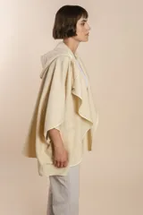 Ruana color crudo de lana fina sin teñir, con capucha, bolsillos y terminaciones envivadas. Tiene un broche para usar cerrada. Es una prenda oversize sin forro, cómoda, versátil y fácil de combinar.
