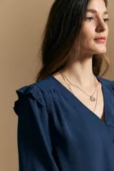 Camisa negra de manga larga con escote en V y cierre frontal de botones. Presenta detalles de volados en los hombros, frunces en la espalda y puños elastizados que le otorgan una silueta relajada y fluida.