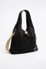 Bolso de mano grande tipo tote bag, color negro, confeccionado en nylon con un bolsillo exterior de red. Posee doble asa de mano y una correa ajustable de tejido color beige. Incluye herrajes metálicos y etiqueta de piel grabada.