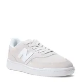Championes urbanos New Balance modelo 080, color gris claro con detalles en blanco. Presentan una combinación de gamuza y malla en la capellada, con el logo "N" distintivo en los laterales y suela de goma blanca.
