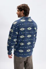 Sobrecamisa de tejido polar con estampa abstracta en tonos azules, verdes y blancos. Presenta cuello camisero, cierre frontal con botones, dos bolsillos frontales con solapa y botones, y un interior afelpado para mayor abrigo.