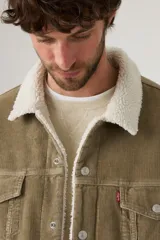 Campera tipo trucker de Levi's en tejido de pana color verde oliva, con forro y cuello de sherpa en color blanco. Presenta cierre frontal con botones metálicos, dos bolsillos en el pecho con solapa y dos bolsillos laterales.
