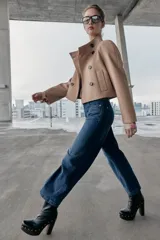 Chaqueta corta de paño en color beige, con cuello subido, manga larga y cierre frontal cruzado con botones oscuros. Presenta bolsillos delanteros de vivo.