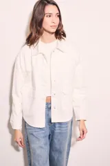 Sobrecamisa color blanco hueso de algodón, con cuello camisero, cierre frontal con botones a presión metálicos, bolsillos de parche en el pecho y bordados florales en los hombros. Corte holgado.