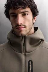 Sudadera con capucha de entrenamiento, confeccionada en tejido técnico de algodón con efecto neopreno. Presenta cierre frontal de cremallera, cuello subido, bolsillos laterales y un bolsillo en el pecho, todos con cierre de cremallera y acabado termofijado.