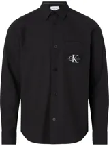 Camisa negra de manga larga Calvin Klein Jeans confeccionada en tejido texturizado de algodón. Presenta cuello camisero, cierre con botones, bolsillo en el pecho con insignia del logo de la marca y puños con botones.