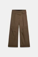 Pantalón de tiro medio color marrón oscuro, estilo cargo, con cintura acabada en vuelta asimétrica, pliegues delanteros y bolsillos laterales y con solapa en las piernas.