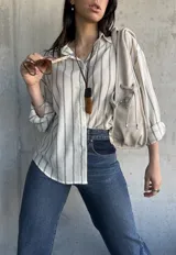 Camisa a rayas verticales color crudo y gris, de corte holgado y mangas largas con puños abotonados.