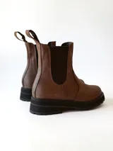 Bota tipo Chelsea de cuero color chocolate, con paneles elásticos laterales, tirador trasero y suela track negra de goma.