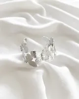 Pulsera rígida plateada con diseño de mariposas caladas.