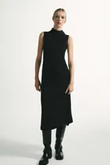 Vestido midi negro con cuello subido y diseño sin mangas (sisa). Presenta un elegante detalle de tejido drapeado en el lateral y cierre trasero con cremallera oculta.