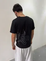 Remera de algodón color negro con estampado gráfico abstracto en tono gris en la parte inferior derecha. Presenta cuello redondo reforzado y corte regular.
