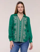 Camisa de estilo boho, color verde, con cuello camisero, escote en V y botonadura frontal con botones perlados. Cuenta con una pechera con bordados geométricos y florales a contraste, mangas largas abullonadas con puños abotonados y delicados bordados dispersos.