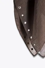 Capa negra de cuello redondo con detalle de tachas plateadas en el ruedo y pañuelo tipo bufanda integrado en el mismo tejido.