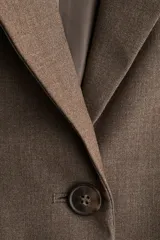 Blazer largo de color marrón, con solapas de muesca, botonadura sencilla y dos bolsillos delanteros con solapa. Presenta forro interior.