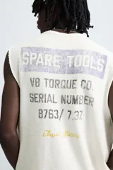 Camiseta sin mangas (manga sisa) de punto color crema, corte relaxed fit, con cuello redondo y acabados irregulares en las sisas. Presenta un texto estampado en el pecho que dice "SERIAL N. 8763/ 7.3Z".