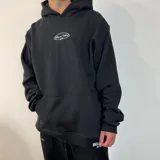 Canguro negro de corte oversize con capucha y bolsillo frontal tipo canguro. Presenta un estampado ovalado blanco en el pecho con la inscripción 'Buena Vibra' y un detalle bordado en el puño de la manga.