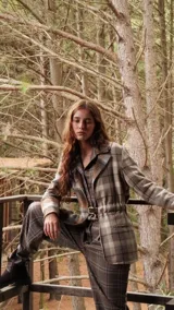 Blazer de largo medio con diseño a cuadros en tonos tierra, confeccionado en mezcla de algodón y poliéster. Presenta solapas clásicas, bolsillos laterales y un cinto de cuero fino incorporado para ajustar la cintura.