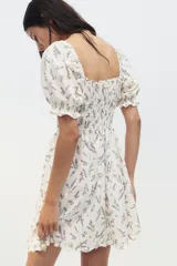 Vestido corto blanco con estampado floral en tonos lavanda, escote cuadrado con volantes, mangas cortas abullonadas con volantes y cuerpo fruncido.