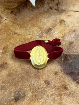 Pulsera elástica de terciopelo marrón con medalla ovalada dorada de la Virgen María.