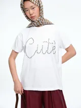 Remera blanca de corte oversize con la palabra 'Cute' escrita en el frente mediante apliques de strass brillantes.