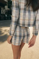 Falda pantalón de tiro alto confeccionada en tejido de tweed con estampado a cuadros en tonos beige, azul y negro. Presenta detalles de falsos botones y cierre lateral con cremallera oculta.
