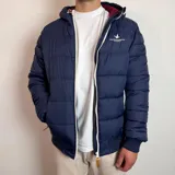 Campera tipo puffer color bordó con capucha, cierre frontal blanco y puños de tejido elástico. Presenta el logo de la marca bordado en el pecho.