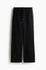 Pantalón negro de corte ancho y recto, con cintura elástica y cordón ajustable. Presenta una fina línea blanca vertical a lo largo de las costuras laterales exteriores.