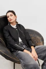 Campera de cuero ovino color negro, con cierre frontal asimétrico, cuello redondo con broche a presión y cierres metálicos en los puños.