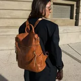 Mochila de eco cuero color suela, de diseño amplio con múltiples bolsillos externos con cierre y tiradores largos. Cuenta con asa superior y correas ajustables.