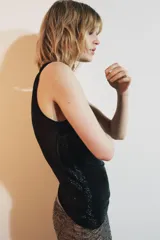 Top negro sin mangas, con cuello redondo y abertura con botón en la espalda. Presenta un detalle de abalorios a tono en el borde del cuello y sisas.