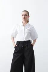 Pantalón wide leg negro de tiro alto con caída fluida y silueta amplia. Presenta cintura alta con botonadura frontal visible.