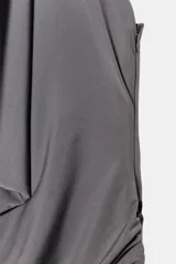 Vestido largo de color negro con cuello halter y detalle de aro metálico en el escote. Presenta un diseño drapeado en la parte frontal y escote en pico pronunciado.