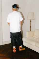 Bermuda de jean color azul oscuro (raw), corte baggy carpintero, con grandes bolsillos frontales y traseros. Presenta un bordado dorado con un monograma en la parte inferior lateral derecha.