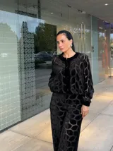 Chaqueta tipo bomber color negro con diseño de patrón geométrico calado y textura aterciopelada. Presenta cuello redondo, cierre frontal con botones y puños elásticos.