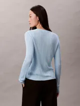 Cardigan de punto canalé con acabado brillante, cuello en V y cierre frontal con botones. Presenta un diseño de manga larga y corte ajustado.