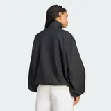 Campera Adidas de corte amplio tipo blouson, color negro con sutil patrón a cuadros. Presenta cuello alto, hombros caídos, mangas voluminosas con puños elastizados y las clásicas tres tiras blancas en los hombros. Incluye el logo del trifolio bordado en el pecho.