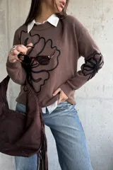Sweater de punto color chocolate con diseño de flores bordadas en hilo negro en el frente y en una de las mangas. Presenta cuello redondo y puños acanalados.