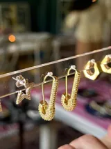 Par de aros dorados con forma de alfiler de gancho, cubiertos de circonias blancas.