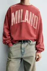 Sudadera de corte boxy fit con cuello redondo y manga larga. Presenta un diseño con efecto lavado y estampado frontal con la palabra Milano en tipografía universitaria a contraste.