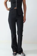 Pantalón negro de tiro medio con corte flare, confeccionado en tejido elasticado. Presenta una costura central y una pequeña abertura en el ruedo. Cierre frontal oculto.